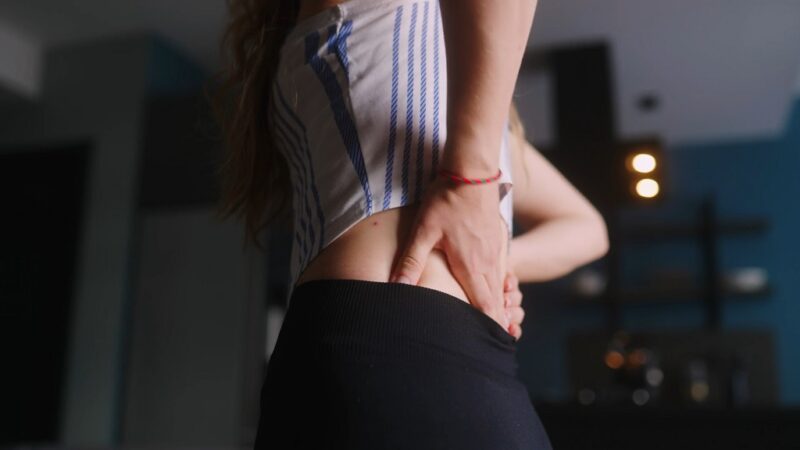 Woman holding her lower back in pain, standing indoors in activewear